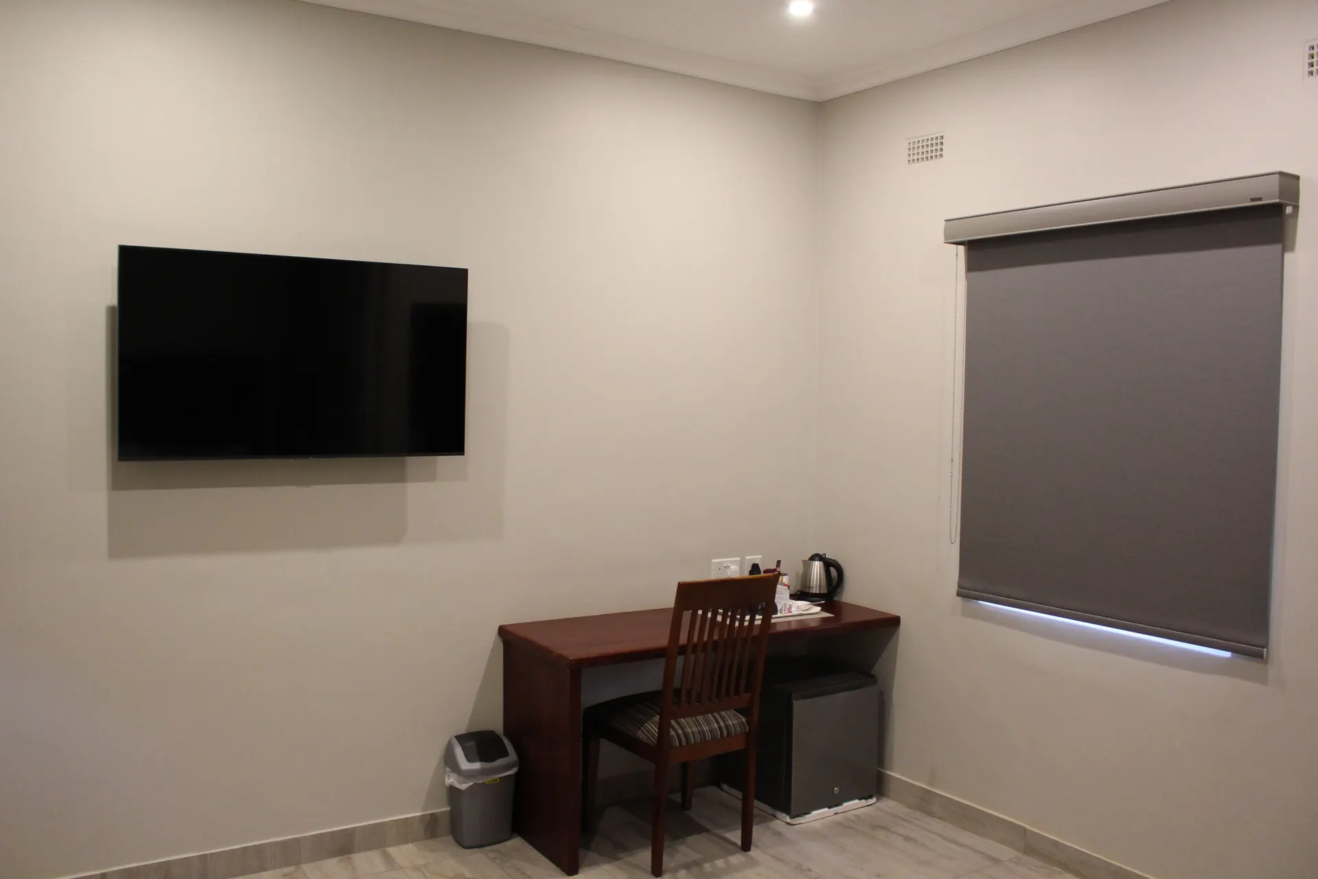 Wall-mounted TV, writing desk with tea and coffee station, and mini fridge in the Basic Room at FIRN Lodge