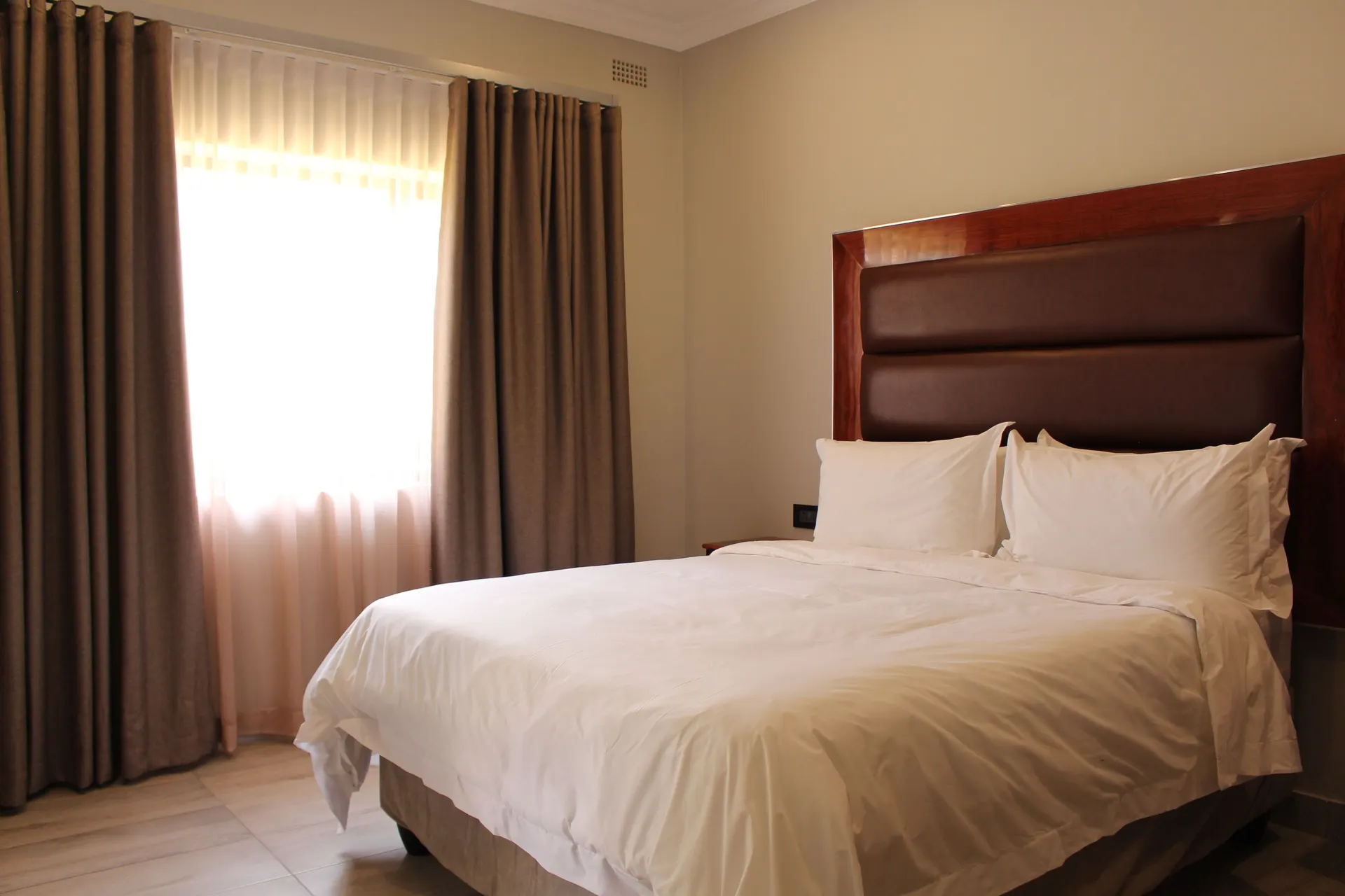 Deluxe Room at FIRN Lodge with a queen bed, leather headboard and sheer-curtained window in daylight