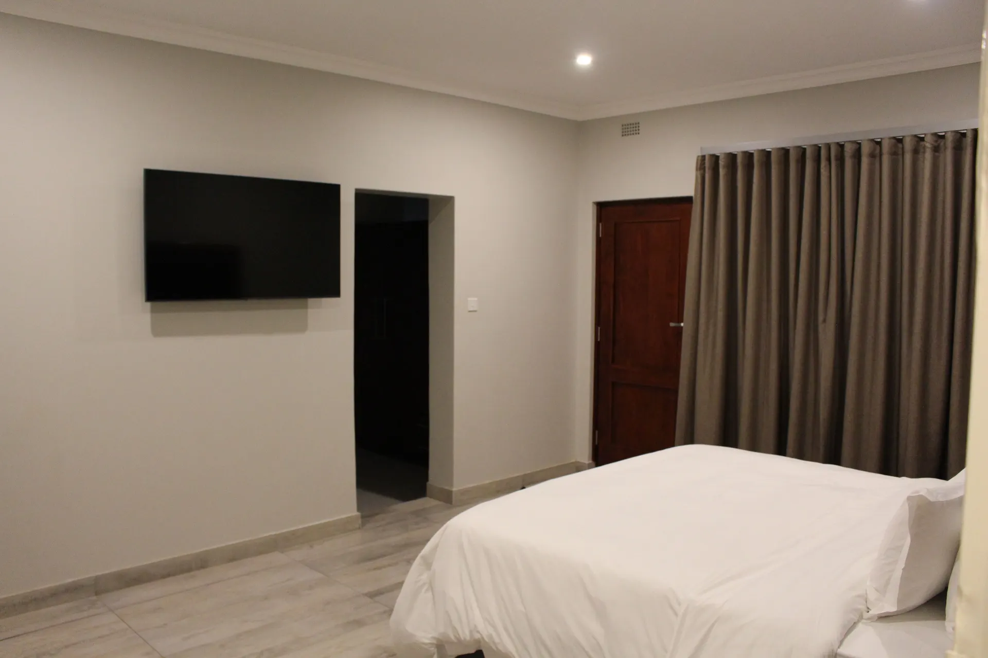 Spacious Executive Room at FIRN Lodge with a wall-mounted TV, doorway to the dressing area and full-length curtains