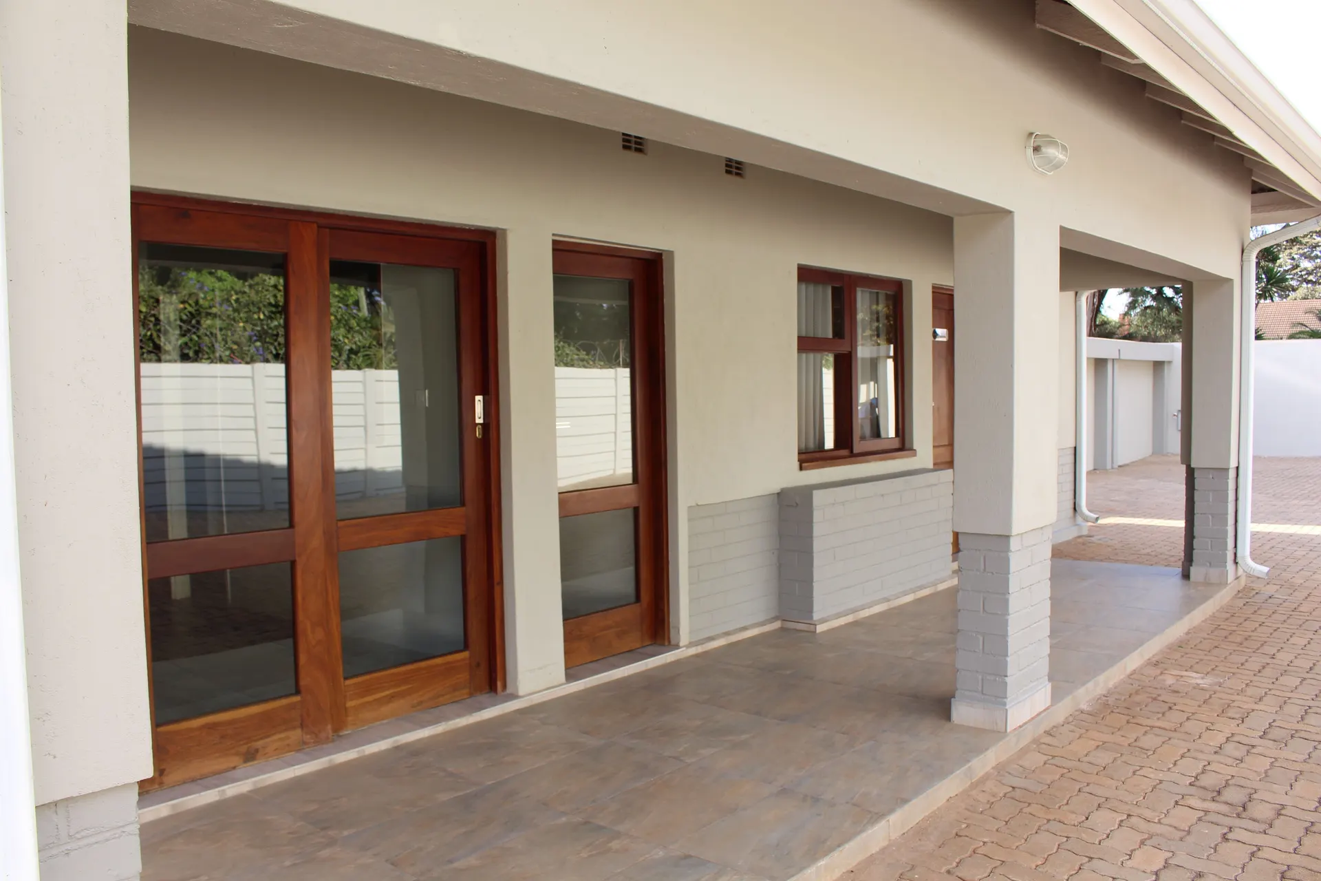 Covered tiled veranda at FIRN Lodge with timber-framed glass sliding doors, a glazed timber door and a window opening onto the paved courtyard