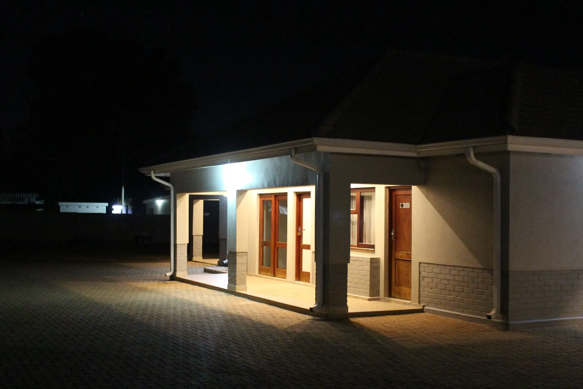 Warmly lit covered porch of a guest-room block at FIRN Lodge at night, with glazed timber French doors and a timber room door