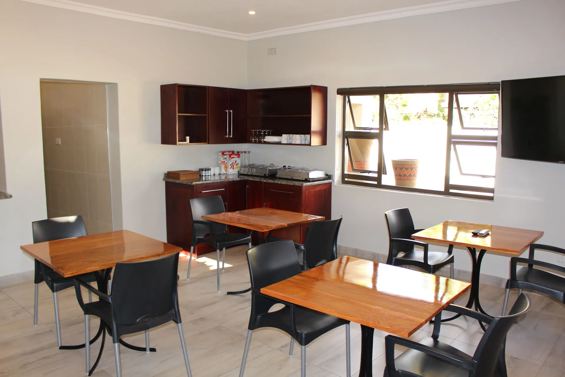 Bright breakfast room at FIRN Lodge with polished timber tables, black chairs and a mahogany kitchenette holding the breakfast buffet