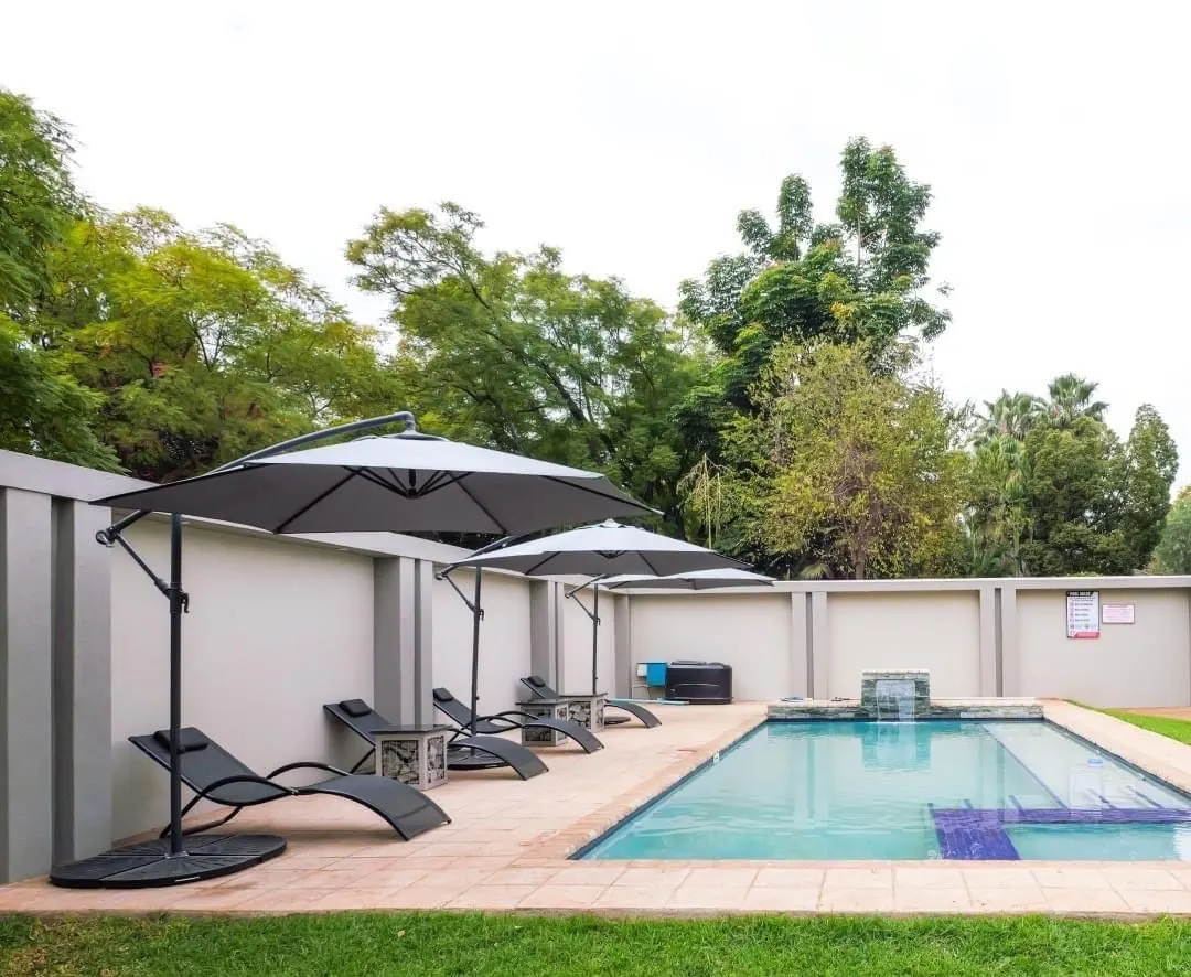 The swimming pool at FIRN Lodge, Harare, with sun loungers under grey umbrellas beside a green lawn