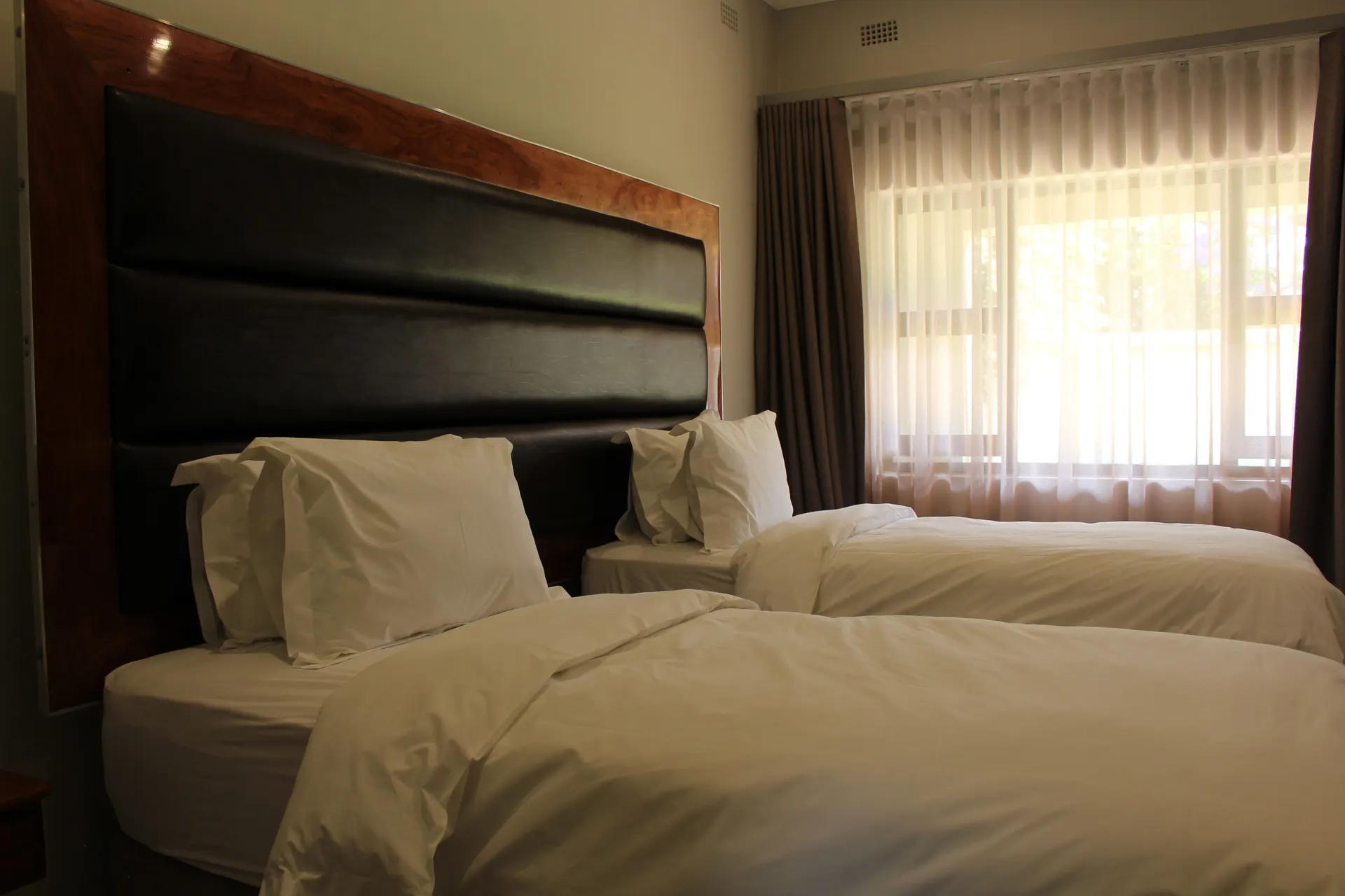 Poolside Twin Room at FIRN Lodge with two single beds beside a large sheer-curtained window in daylight