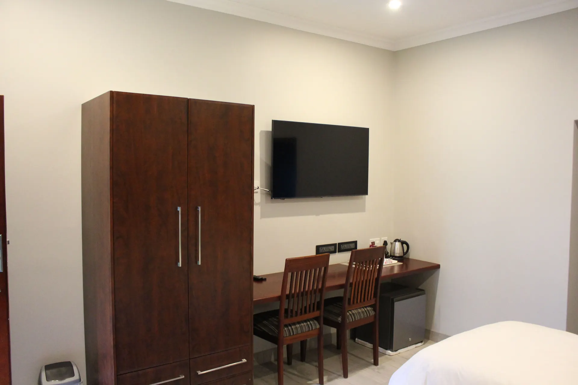 Wardrobe, wall-mounted TV and long desk with two chairs in the Poolside Twin Room at FIRN Lodge
